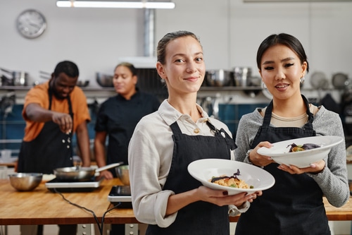 two wait staff wearing aprons and holding gourmet dishes ready to serve after taking food handler training