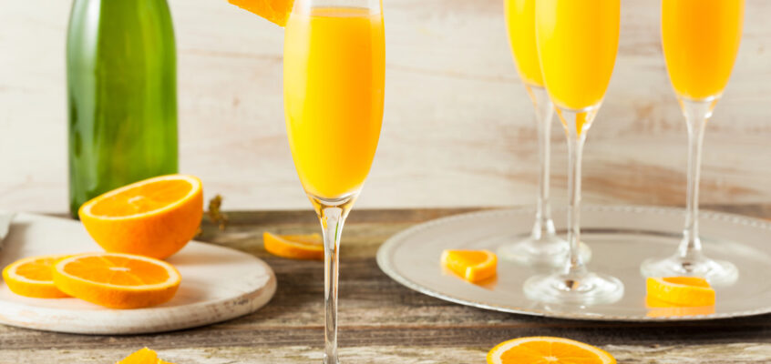 Classic orange juice mimosa in a tall flute with a fresh orange wheel garnish and bubbles
