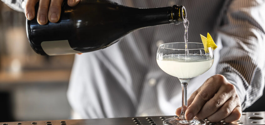A crisp, backlit French 75 cocktail in a classic champagne flute with bubbles rising and a long, elegant lemon spiral garnish.
