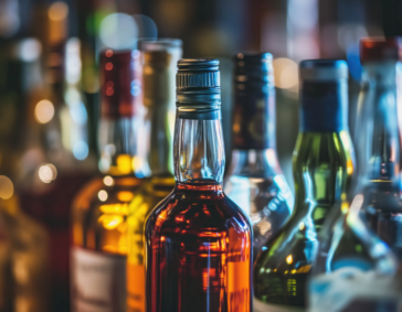 A close-up, shallow depth-of-field shot of several liquor bottles on a bar, with one central bottle of amber spirits in sharp focus.