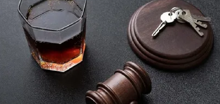 A judge's gavel and car keys on a desk with a glass of amber liquor in the background.