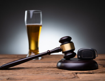 A wooden judge's gavel and a car key fob on a wooden table, with a tall glass of beer in the blurred background.