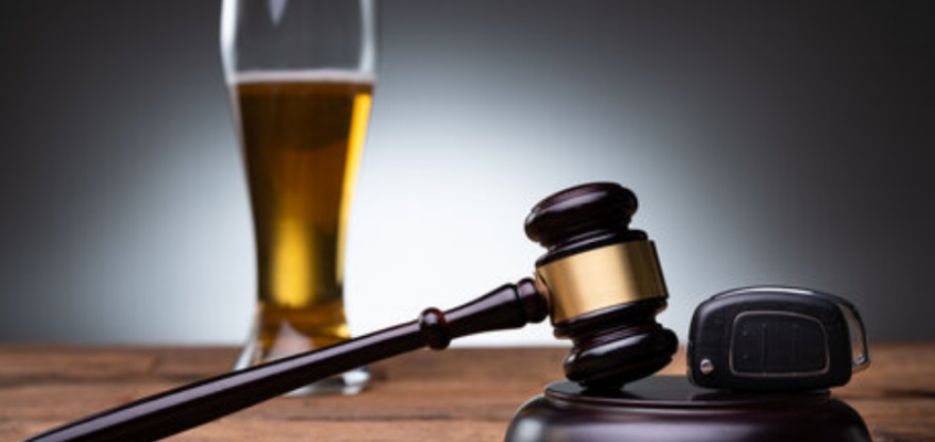 A wooden judge's gavel and a car key fob on a wooden table, with a tall glass of beer in the blurred background.
